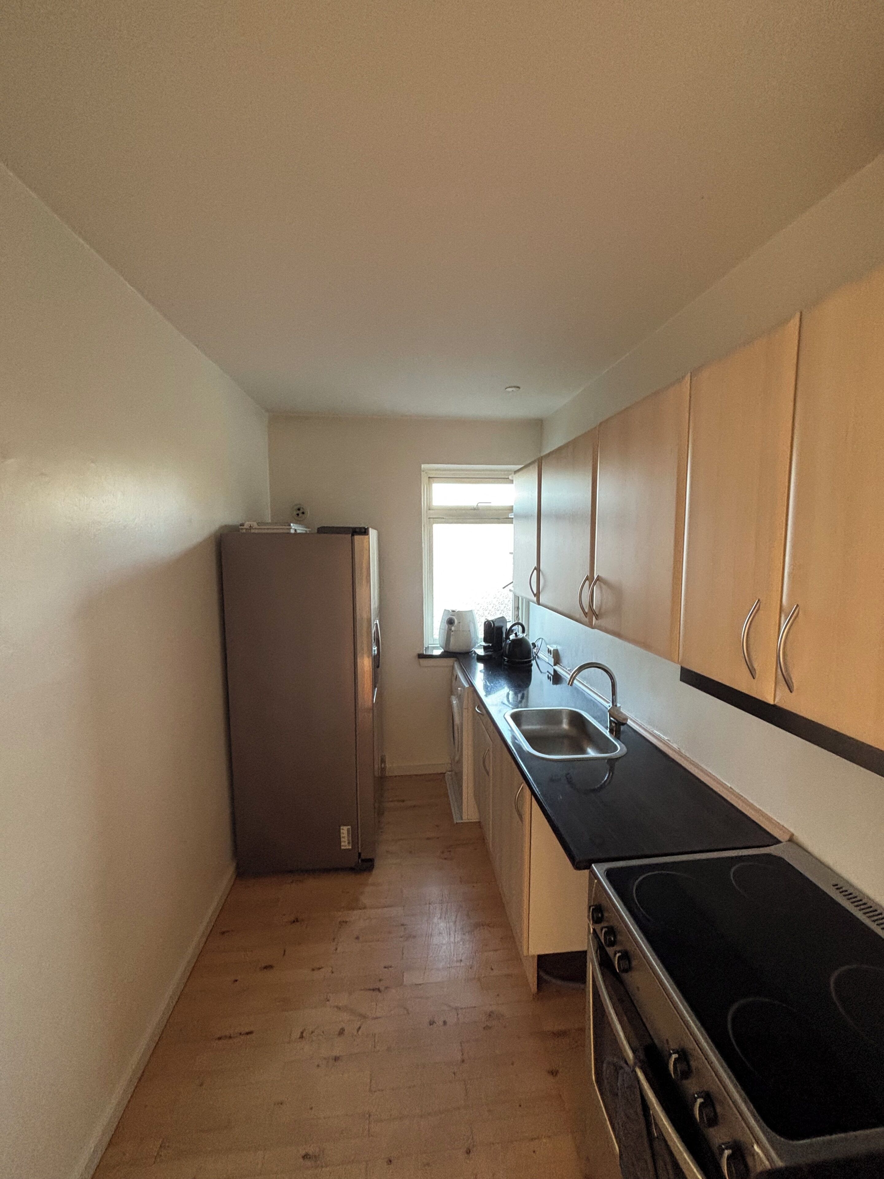 A compact kitchen with a refrigerator, stove, sink, and wooden cabinets.