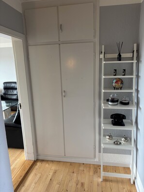Um quarto com um guarda-roupa, uma estante branca com objetos decorativos e um sofá preto.