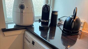 A compact kitchen with a washing machine, a coffee maker, and a kettle on the countertop.