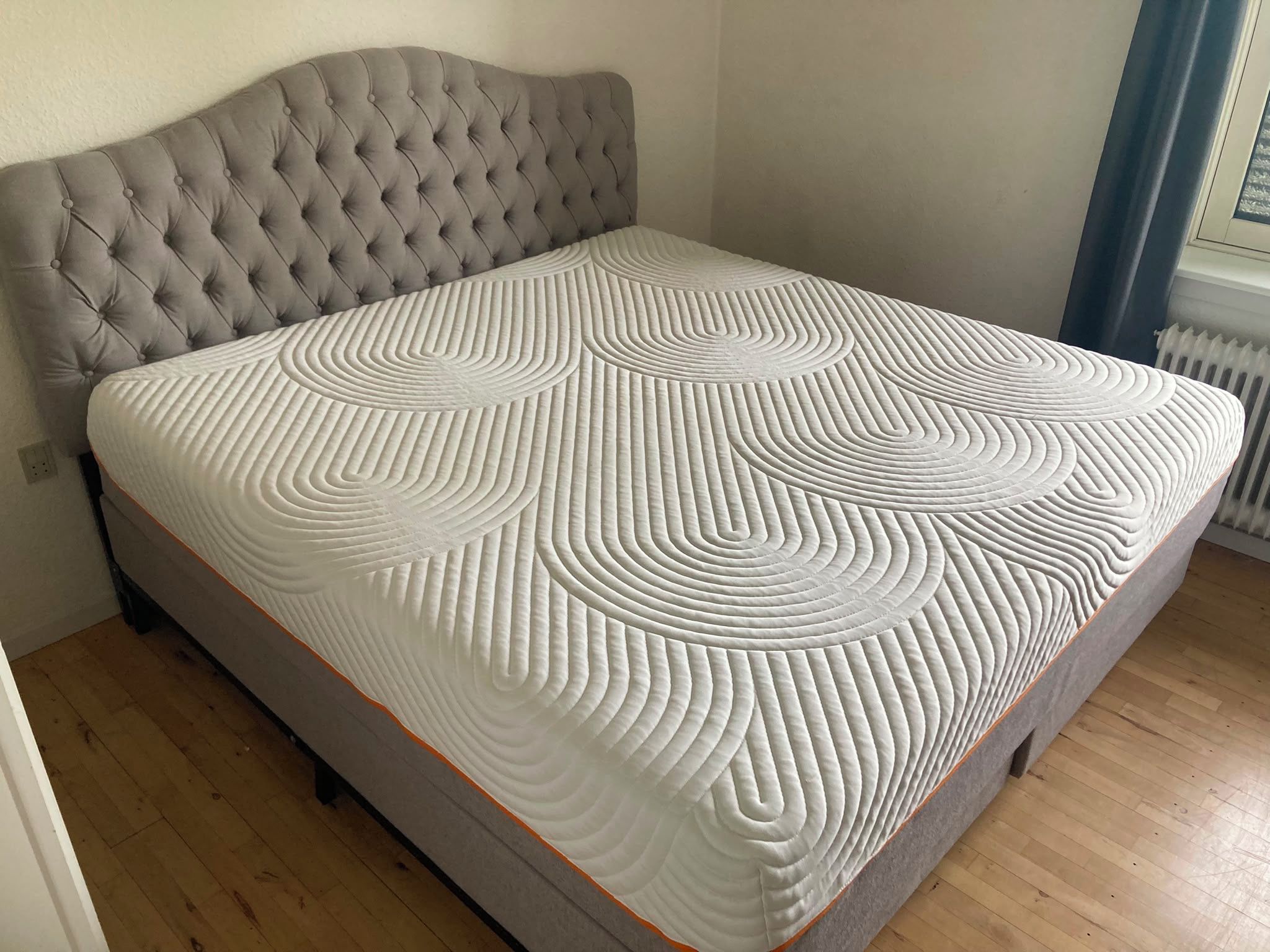 Ein Bett mit einer gesteppten Kopfteil und einer gemusterten Matratze.