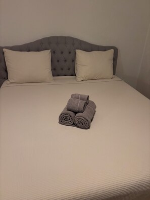 Cama com cabeceira estofada, duas almofadas e uma toalha enrolada.