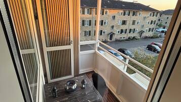 A balcony with a table and chairs, a view of a residential building, and a clear sky.