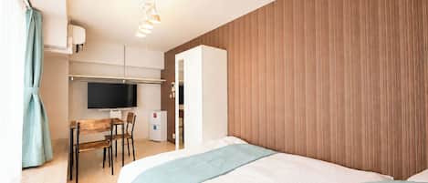 A hotel room with a bed, a desk with a chair, a television, and a wardrobe.
