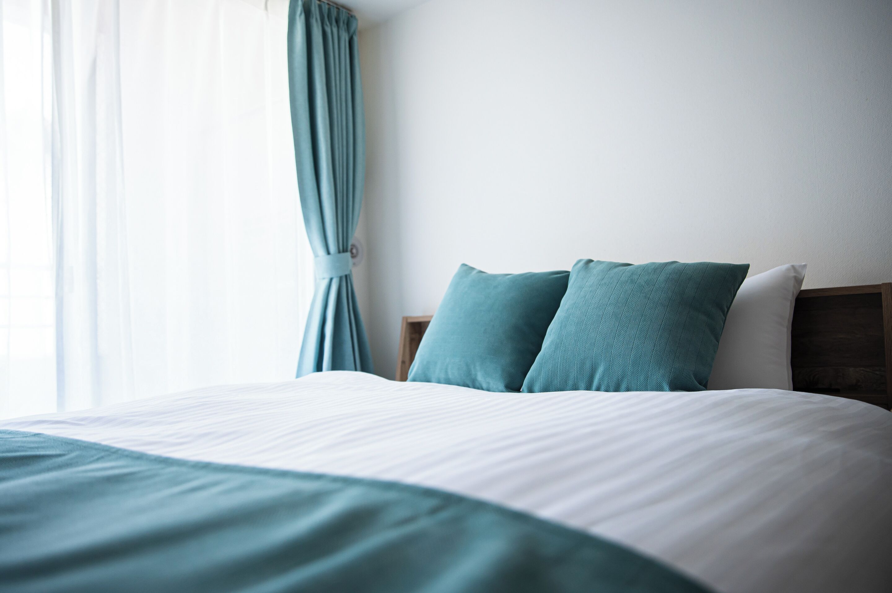 A neatly made bed with a white and teal bedspread, two teal pillows, and a wooden headboard.