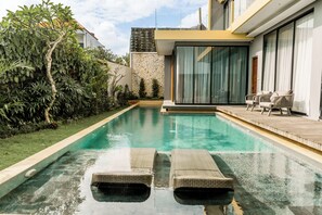 Ein moderner Pool mit klarem Wasser, umgeben von Grün und einer Holzterrasse.