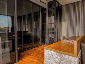 Un interior modern amb un taulell de recepció de fusta, una porta de vidre que dona a un balcó, i una vista de l'horitzó urbà.