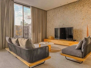 Ein modernes Wohnzimmer mit Sofa, Sessel und einem Flachbildfernseher auf einer Holzkonsole.