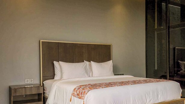 Un dormitorio moderno con cabecera de madera, cama con ropa blanca y mesita de noche con lámpara.