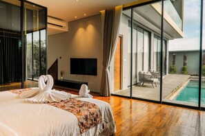 Ein modernes Hotelzimmer mit einem großen Bett, einem Flachbildfernseher, einem Balkon mit Pool und Blick ins Freie.