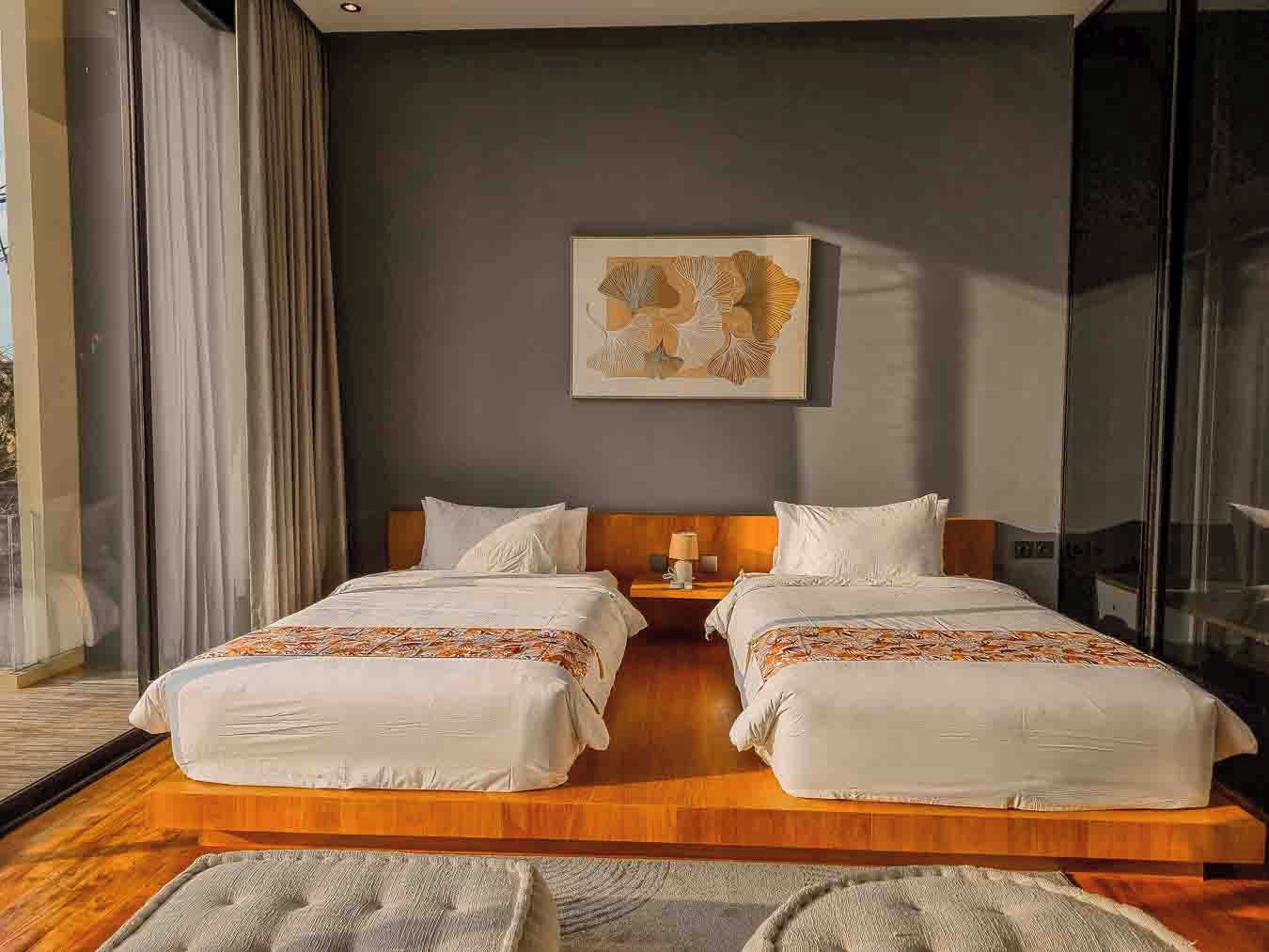 A double bed with a wooden headboard, a bedside table with a lamp, and a large window with curtains.
