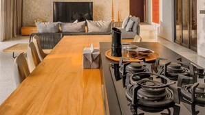 Un comedor moderno con una mesa de madera larga, una estufa a gas empotrada y un televisor al fondo.