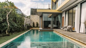 Una piscina moderna con cubierta de madera y puertas de cristal que dan a un dormitorio.