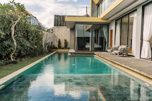 Ein moderner Pool mit Holzterrasse und Glastüren zu einem Schlafzimmer.