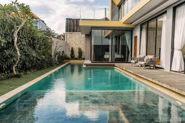 Ein moderner Pool mit Holzterrasse und Glastüren zu einem Schlafzimmer.