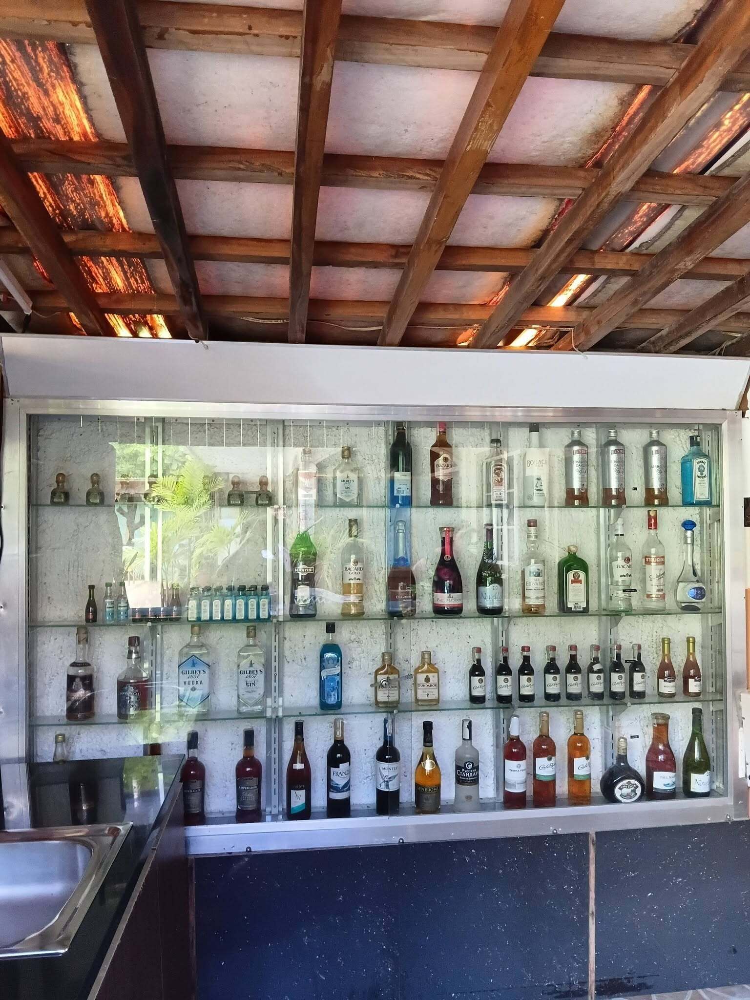 Zona de bar con techo de madera y vitrina de vidrio llena de diferentes botellas de licor.