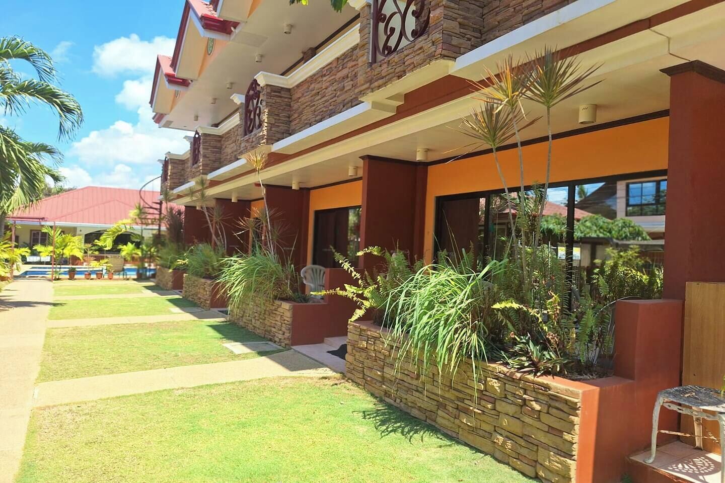 Un hotel con fachada de piedra, varios balcones y un jardín cuidado con diversas plantas.