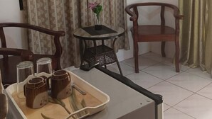 Una habitación pequeña con una mesa de comedor, dos sillas, una mesita con un florero y una bandeja con tazas y una cuchara.