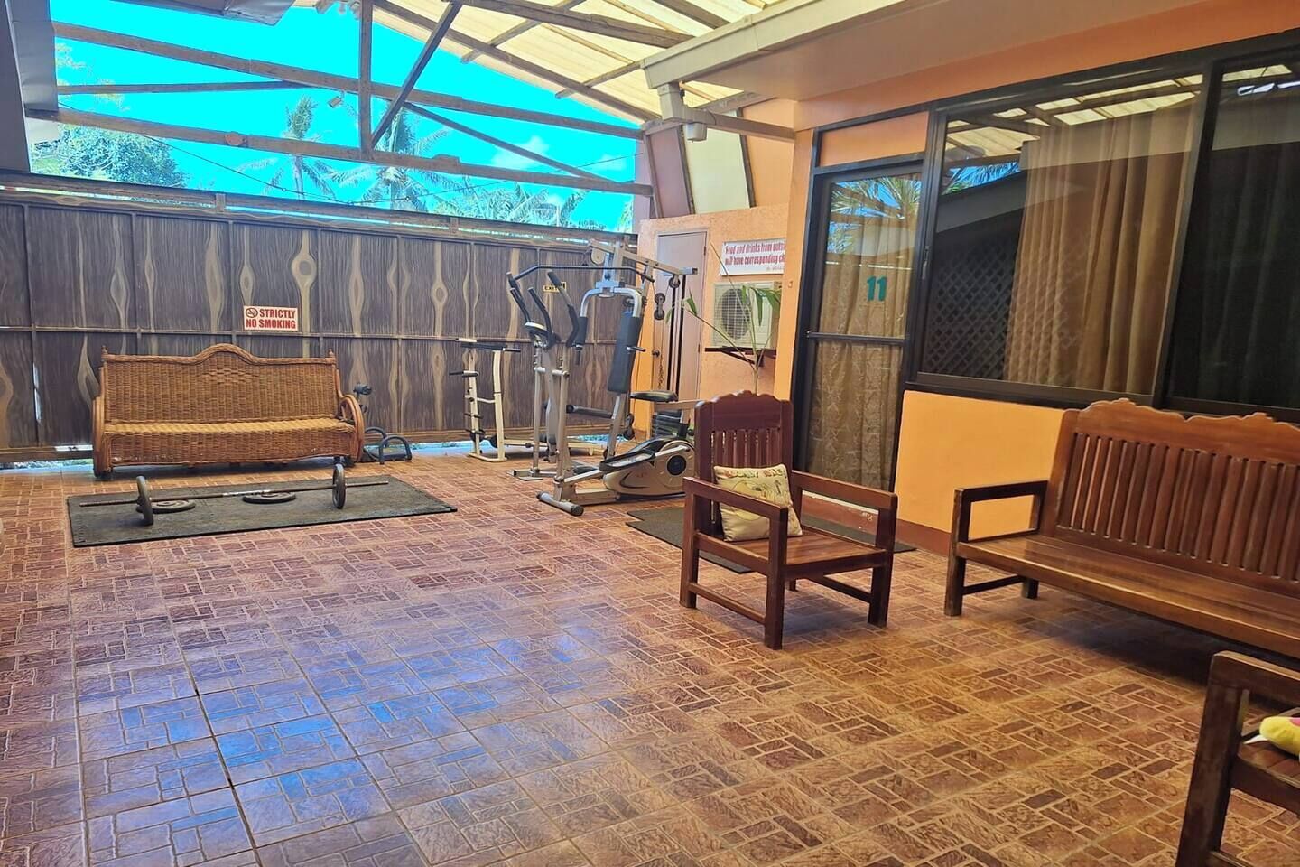 Un espace de remise en forme en plein air équipé de matériel d’exercice, d’un banc en bois et d’un panneau indiquant qu’il est interdit de fumer.