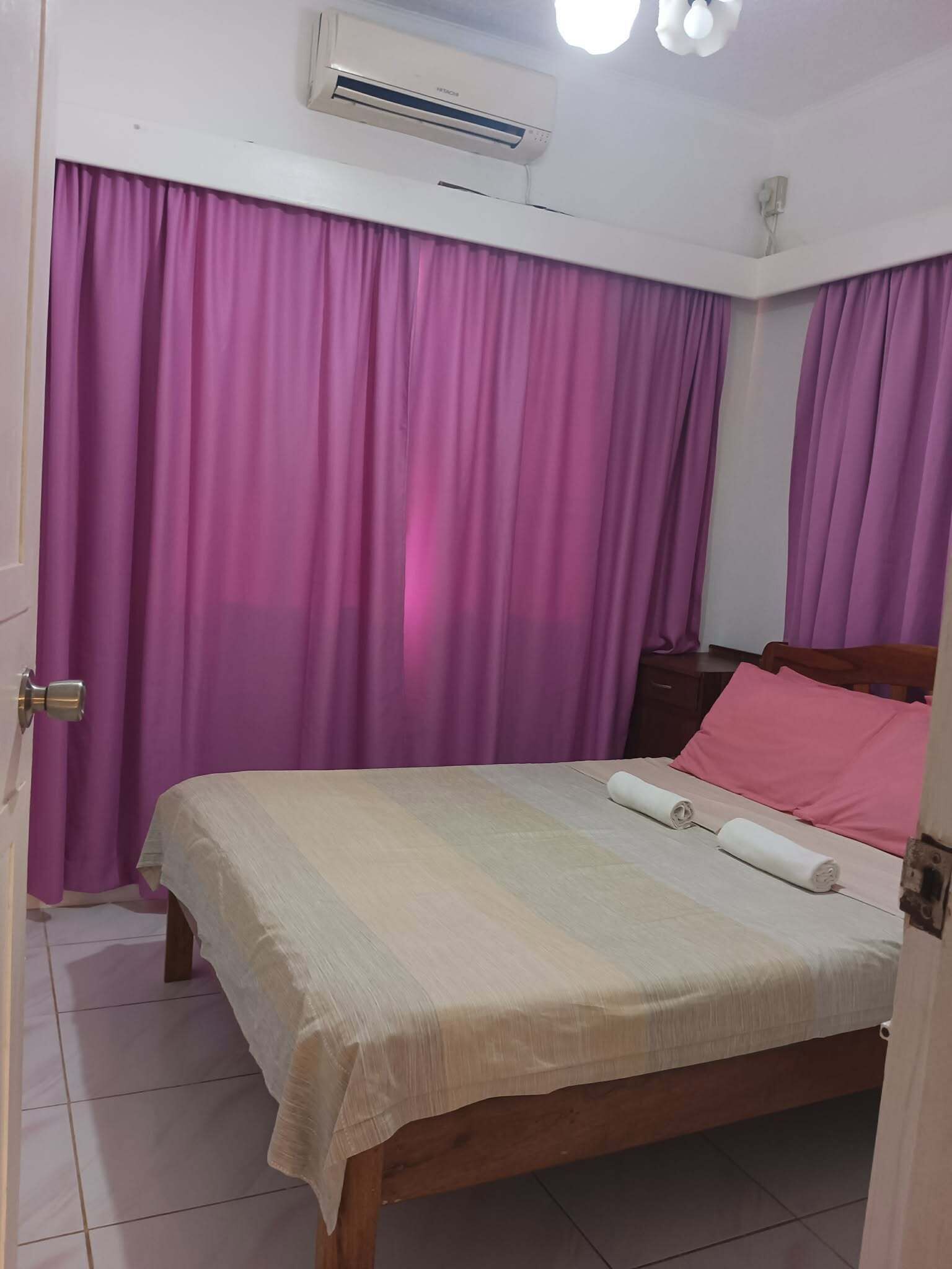 A bedroom with a bed, curtains, an air conditioning unit, and a wooden headboard.