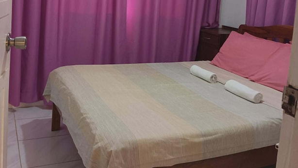 Un dormitorio con cama, cortinas, un equipo de aire acondicionado y un cabecero de madera.