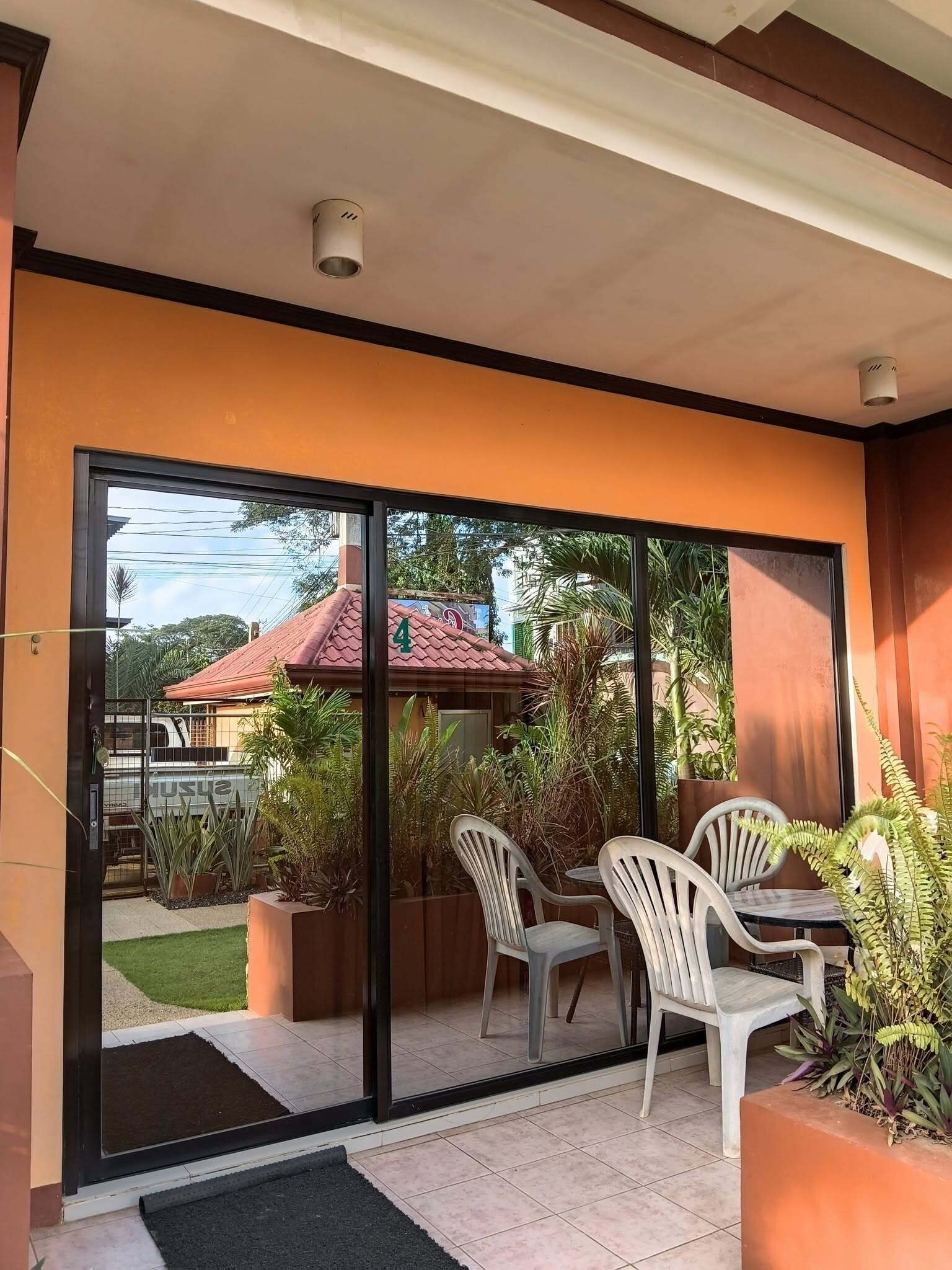 A modern outdoor patio with a glass door leading to a garden, a table with chairs, and potted plants.