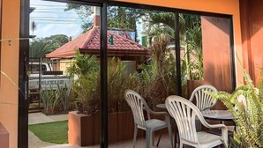 Un patio exterior moderno con puerta de vidrio que da a un jardín, una mesa con sillas y plantas en macetas.