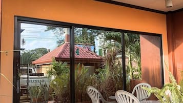 A modern outdoor patio with a glass door leading to a garden, a table with chairs, and potted plants.