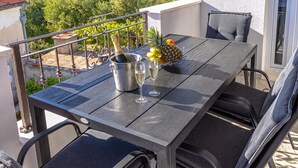 A balcony with a table set for two, featuring a bottle of champagne, two glasses, and a fruit bowl with pineapple and oranges. - Apartment With Balcony And Parking 2, Okrug Gornji, Croatia (Okrug Gornji)