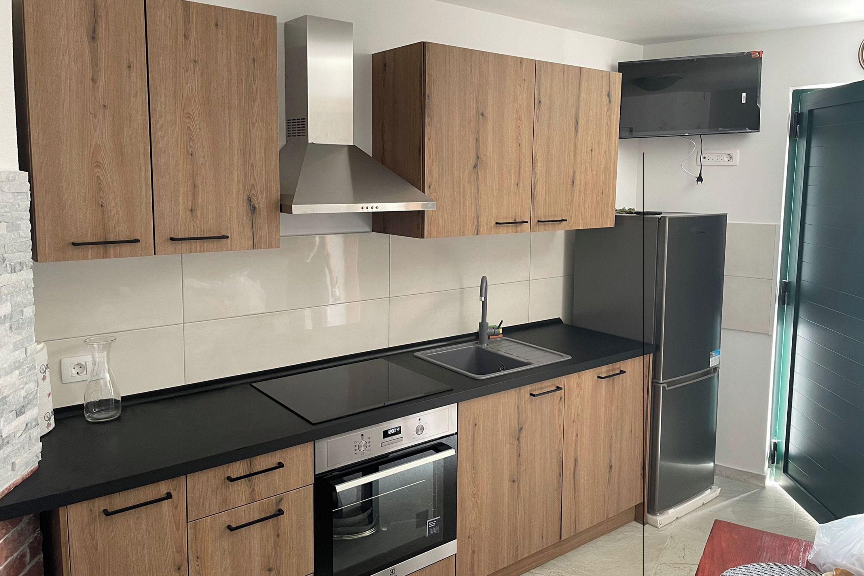 A modern kitchen with wooden cabinets, a stainless steel range hood, a built-in oven, a double sink, and a refrigerator.