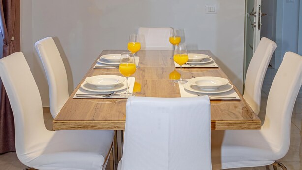 A dining table set with white chairs, plates, and glasses of orange juice. - Apartment With Balcony And Parking 1, Okrug Gornji, Croatia (Okrug Gornji)