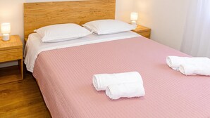 A neatly made bed with a pink bedspread and two pillows, two bedside lamps, and two rolled towels on the bed. - Apartment With Balcony And Parking 1, Okrug Gornji, Croatia (Okrug Gornji)