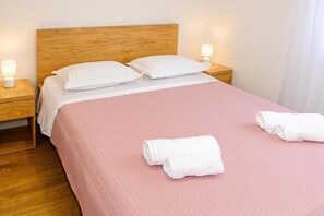 Ein ordentlich bezogenes Bett mit einer rosa Tagesdecke, zwei Kissen, zwei Nachttischlampen und zwei aufgerollten Handtüchern.