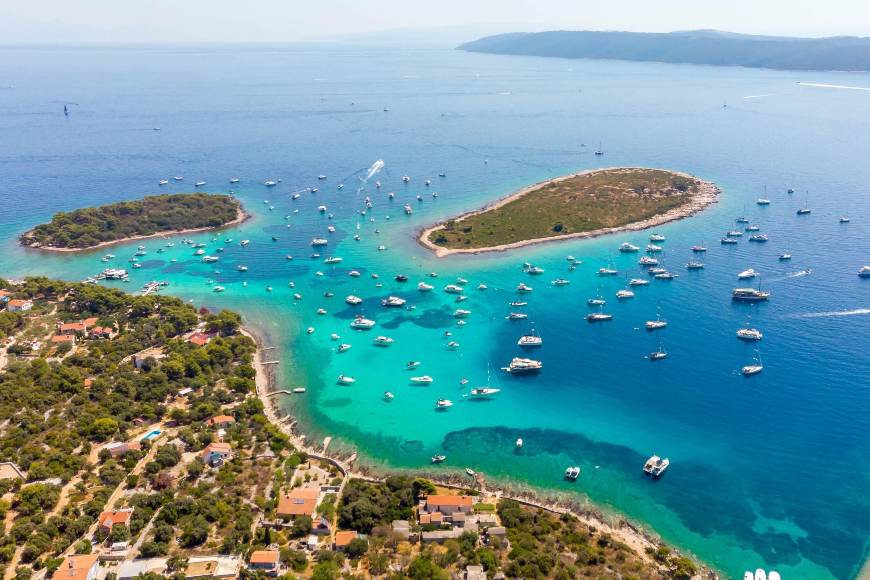 An aerial view of a coastal area with numerous boats, clear turquoise waters, and a small island with a heart-shaped coastline.