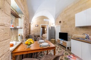 A compact kitchen with a dining area, stone walls, a TV, and a refrigerator. - NonnAnna Apartment In Martano Historic Centre, Martano, Italy (Martano)