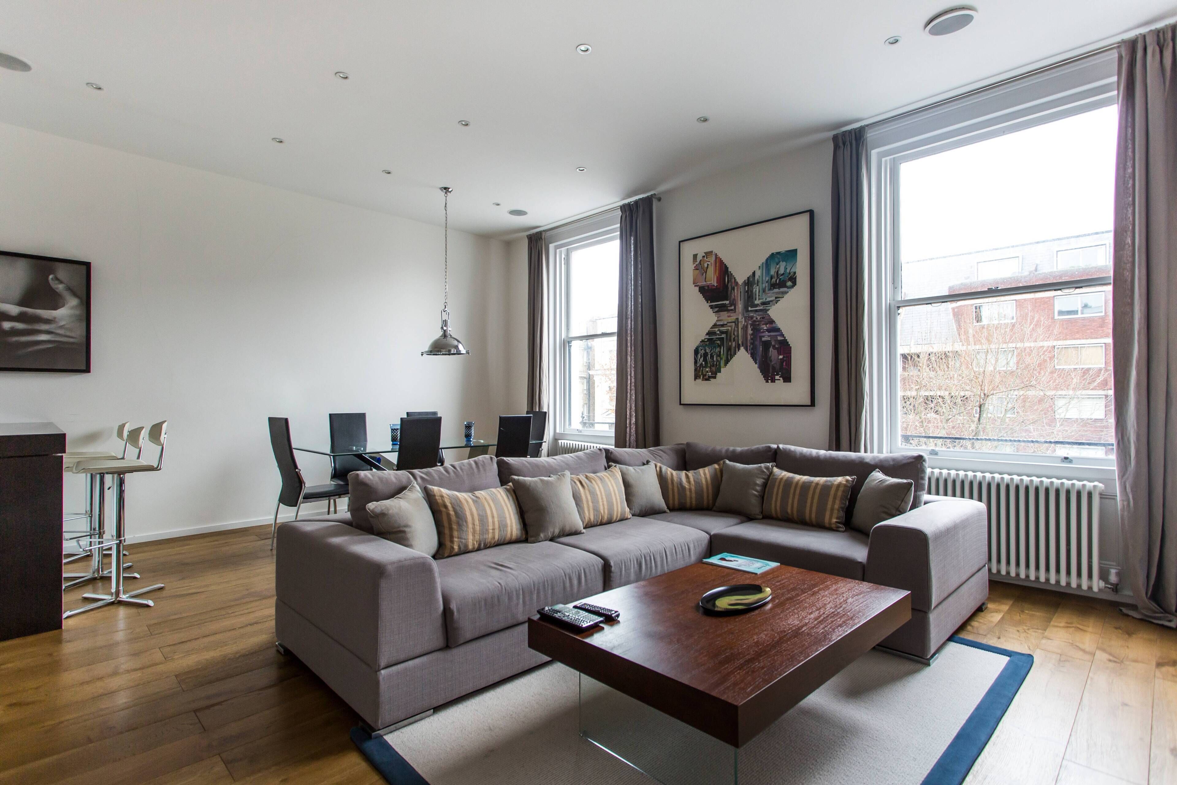 A modern living room with a sectional sofa, a coffee table, and a dining area with a desk and chairs.