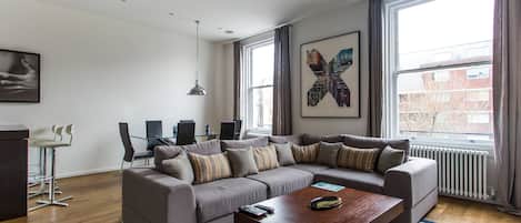 A modern living room with a sectional sofa, a coffee table, and a dining area with a desk and chairs.