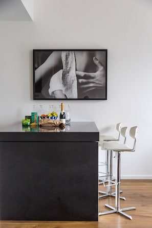 Eine moderne Bar mit einer schwarzen Arbeitsplatte, einem Bilderrahmen mit einem Schwarz-Weiß-Foto sowie einer Auswahl an Snacks und Getränken.