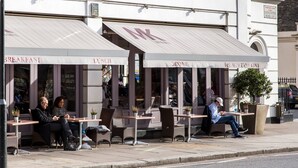 Kahvila, jossa on ulkotilojen istumapaikkoja, ja sen edessä on kyltti, josta ilmenee, että se sijaitsee Gloucester Roadilla. Lisäksi kahvilan puhelinnumero on näkyvillä.