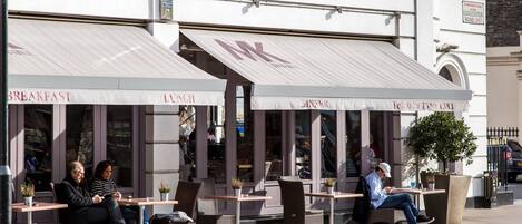 A cafe with outdoor seating, a sign indicating it is on Gloucester Road, and a telephone number.