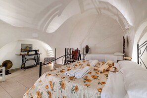 Ein Schlafzimmer mit einem blumigen Bettüberwurf, einer Nähmaschine, einem Sessel und einem Bett mit weißen Leinen.