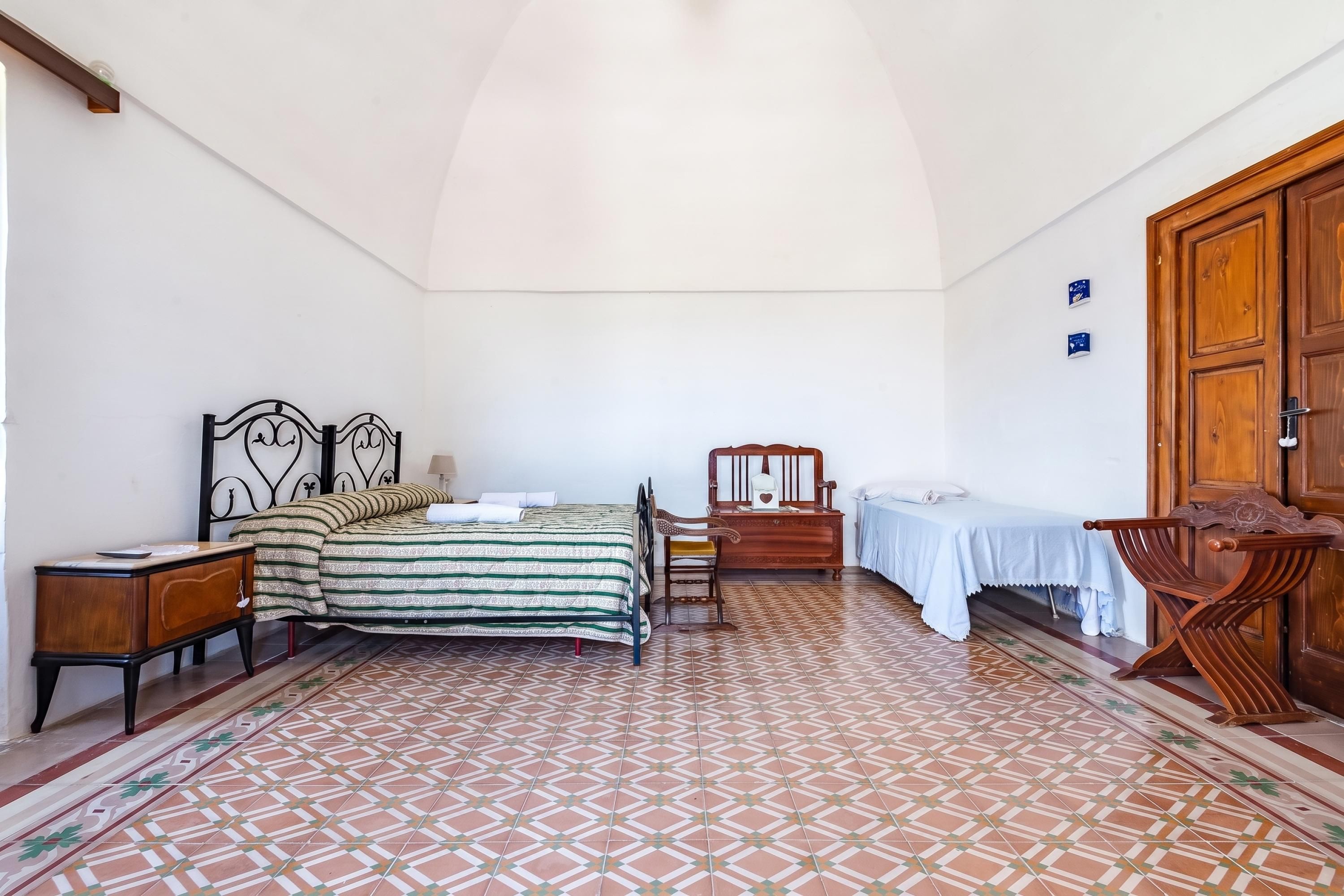 Un dormitorio con una cama, mesitas de noche, un armario de madera, una silla y una pequeña mesa con mantel.
