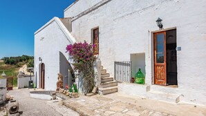 A white building with a wooden door, a staircase, and a small garden with purple flowers. - Masseria Le Mesolecchie, Crispiano, Italy (Crispiano)