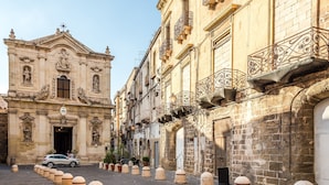 A historic building with ornate architectural details, a paved street, and bollards lining the sidewalk. - Masseria Le Mesolecchie, Crispiano, Italy (Crispiano)