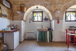 Una cocina con un refrigerador blanco, un lavamanos con un paño verde, una silla roja y una ventana con cortinas.