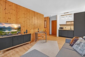 A modern living room with a wooden wall, a TV, a dining area, and a kitchen. - L'Anemone near Campo Smith Lifts, Bardonecchia, Italy (Bardonecchia)