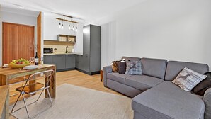 A modern living room with a grey sofa, wooden dining table, and a kitchen area in the background. - L'Anemone near Campo Smith Lifts, Bardonecchia, Italy (Bardonecchia)