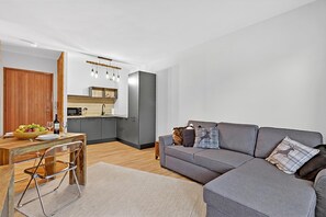 A modern living room with a grey sofa, wooden dining table, and a kitchen area in the background. - L'Anemone near Campo Smith Lifts, Bardonecchia, Italy (Bardonecchia)