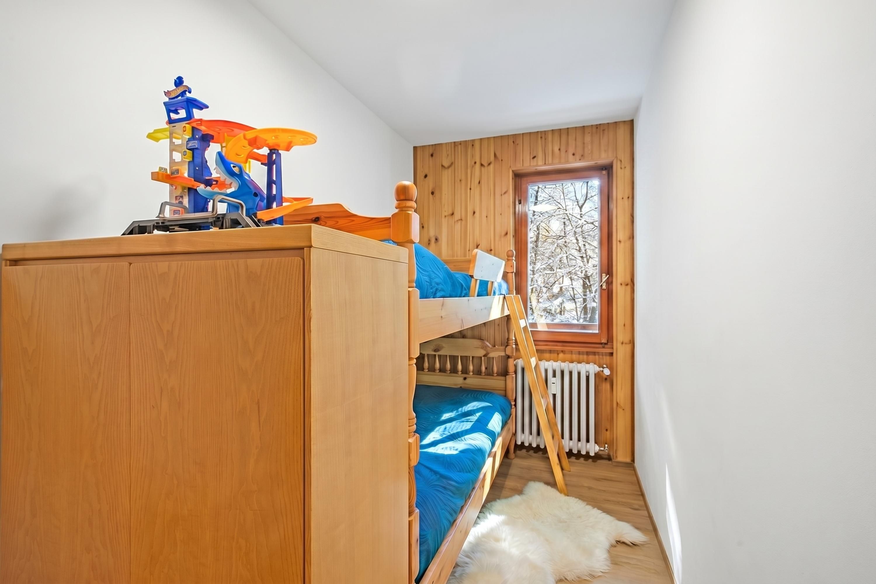 A bunk bed with a toy car and a window with a view of trees.