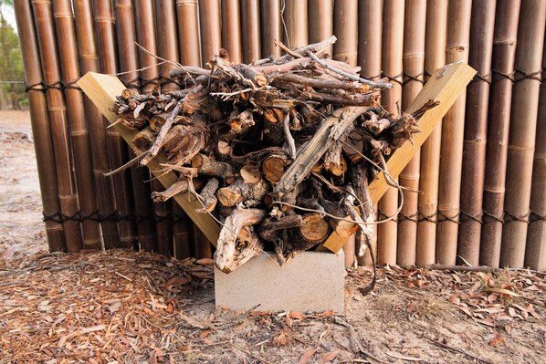 A pile of firewood stacked in a concrete block against a bamboo fence.