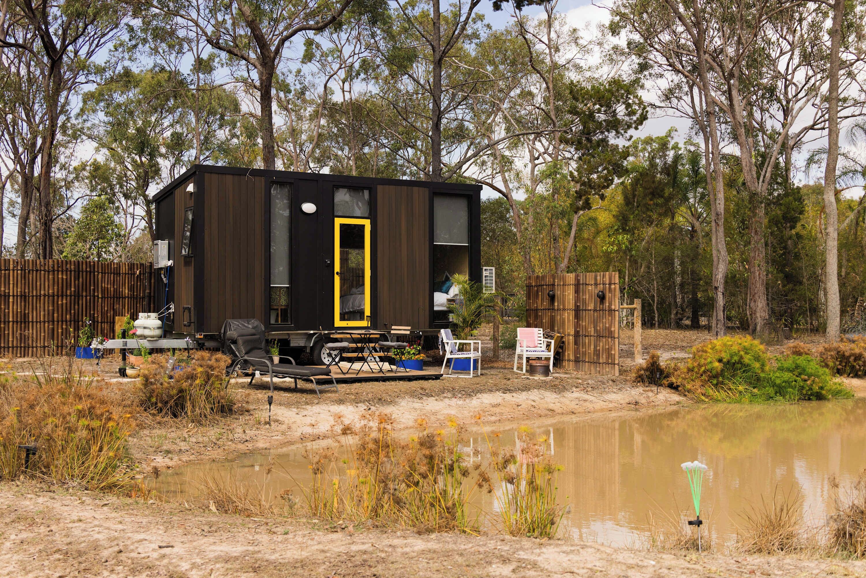 A small cabin with a yellow door, surrounded by a natural landscape with trees and a body of water.